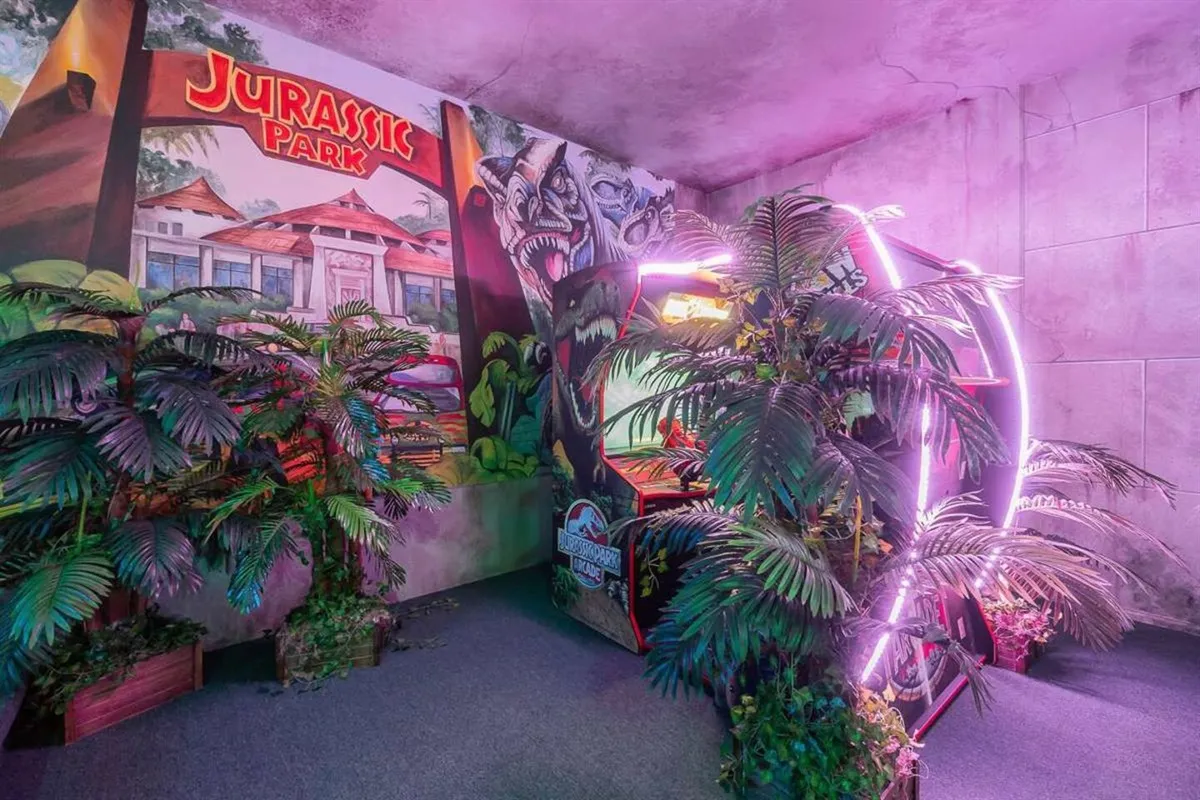 Jurassic Park themed game area with dinosaur mural, tropical plants, and neon ring light
