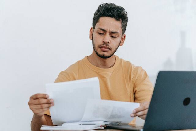 a-property-manager-in-a-yellow-sweater-reviews-documents-at-their-desk-with-a-laptop-nearby
