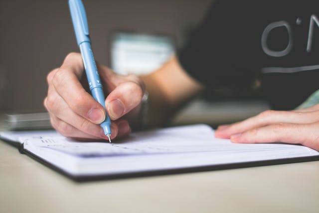 a-person-writing-something-in-a-notebook-using-a-blue-pen