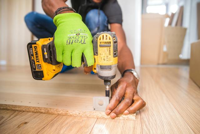 a-person-holding-a-drill-attaching-a-metal-hinge-to-wood