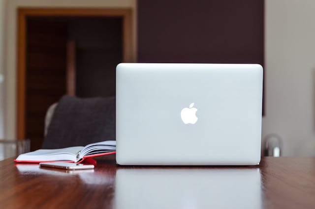 apple-macbook-on-a-wooden-table-with-an-open-notebook-and-smartphone-beside-it