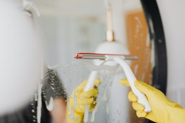 person-wearing-yellow-gloves-using-a-squeegee-to-clean-a-mirror